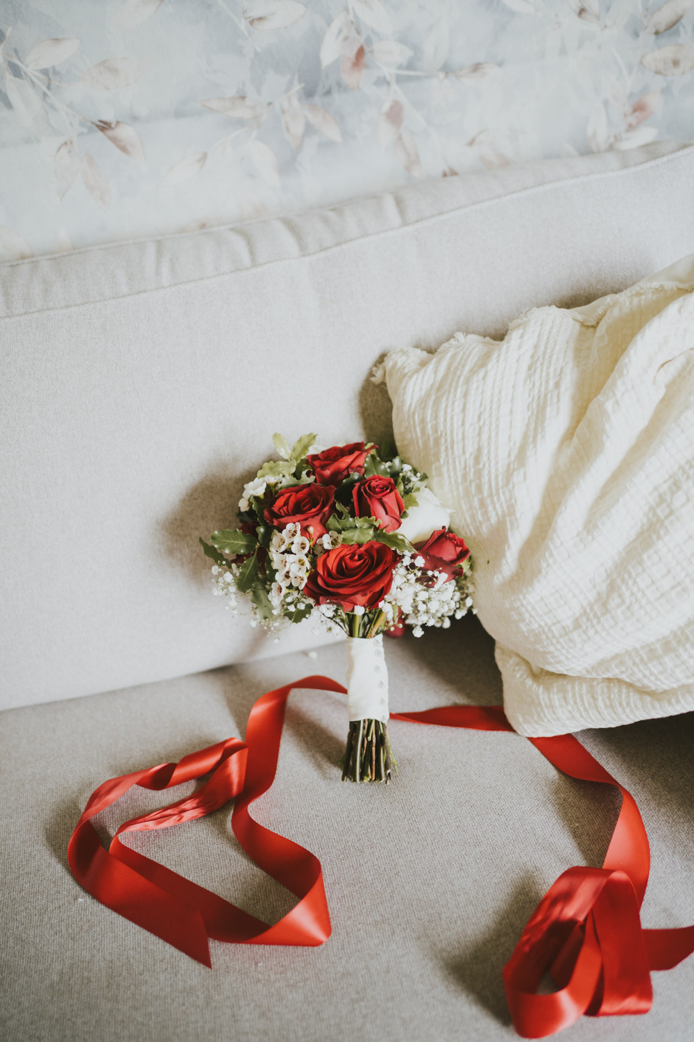 Red bridal bouquet and ribbon arranged on pale upholstery