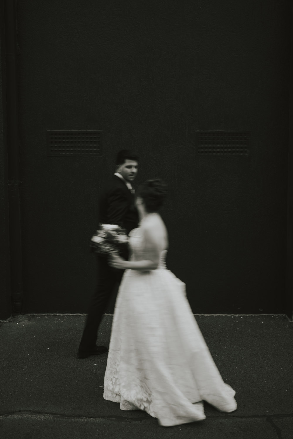 A newlywed couple moving past a dark wall in intentional blur