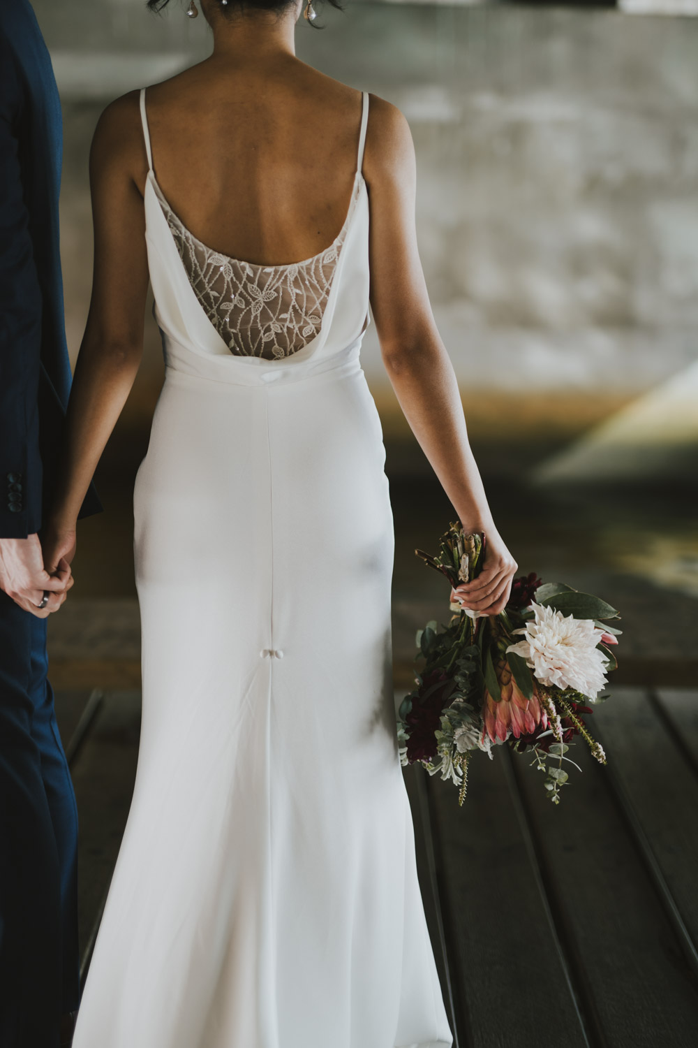 A bride seen from behind holding a sculptural native bouquet beside her partner