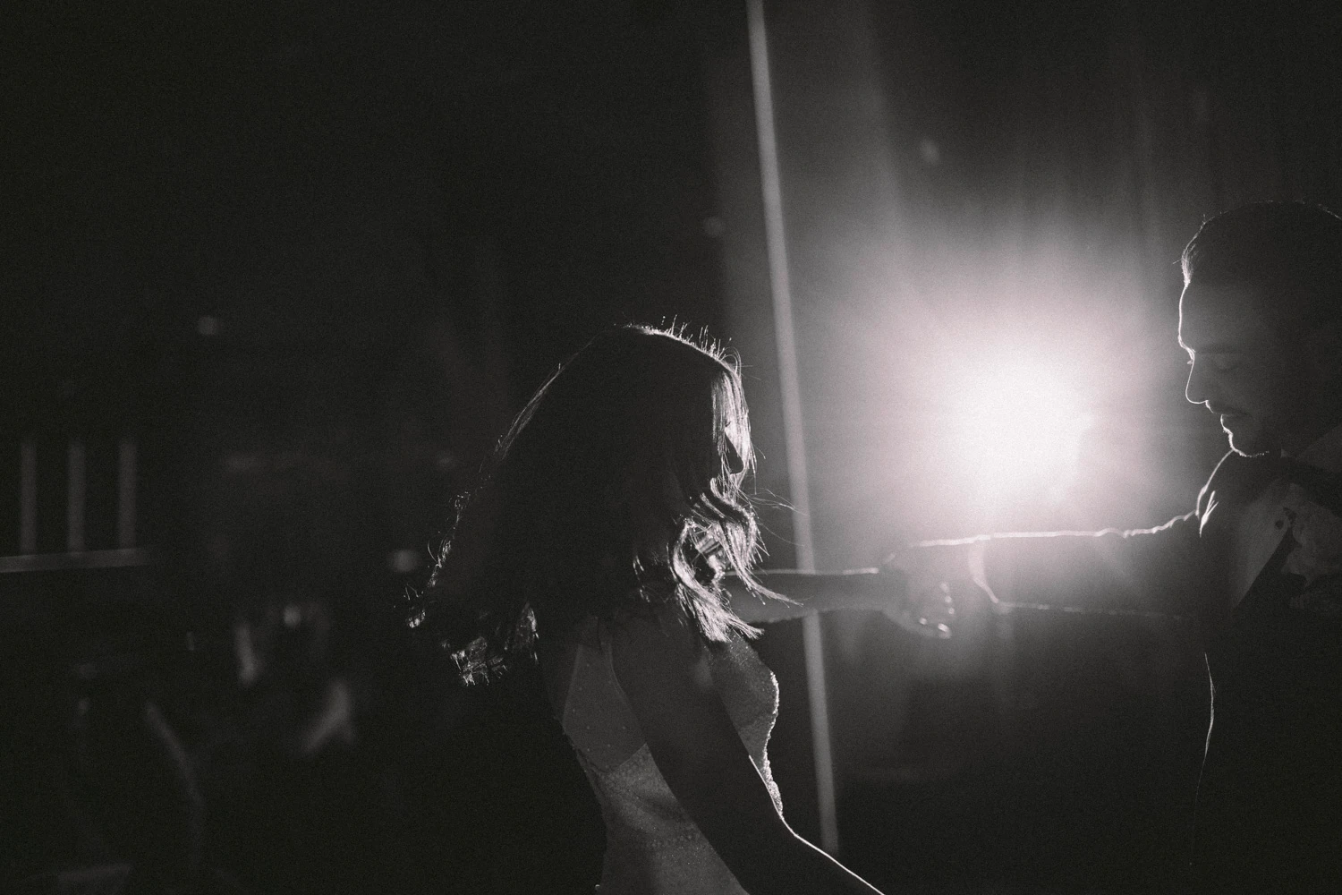 Newlyweds dancing in black and white against a bright reception backlight