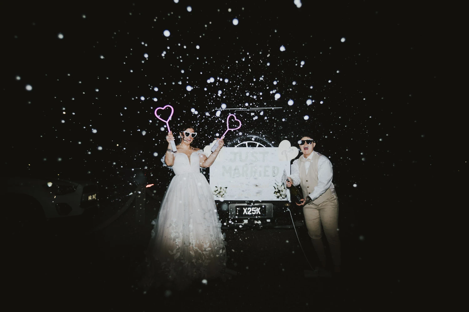 Newlyweds celebrating beneath a storm of white foam beside their just married car