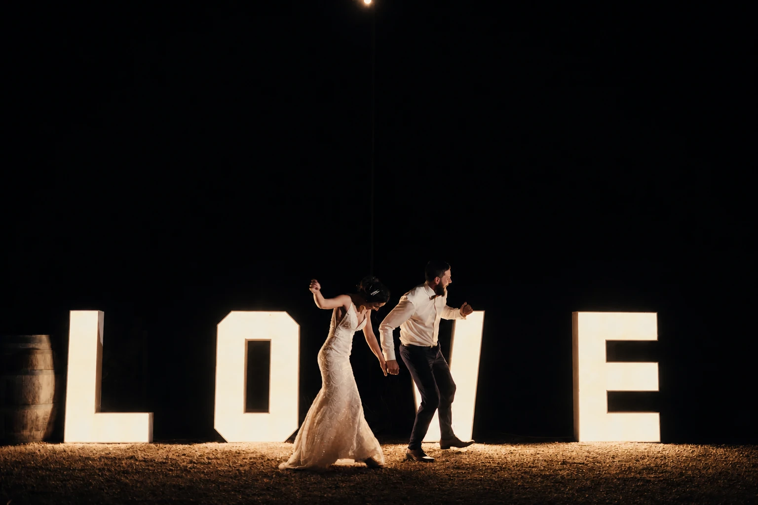 Newlyweds dancing between giant illuminated LOVE letters after dark