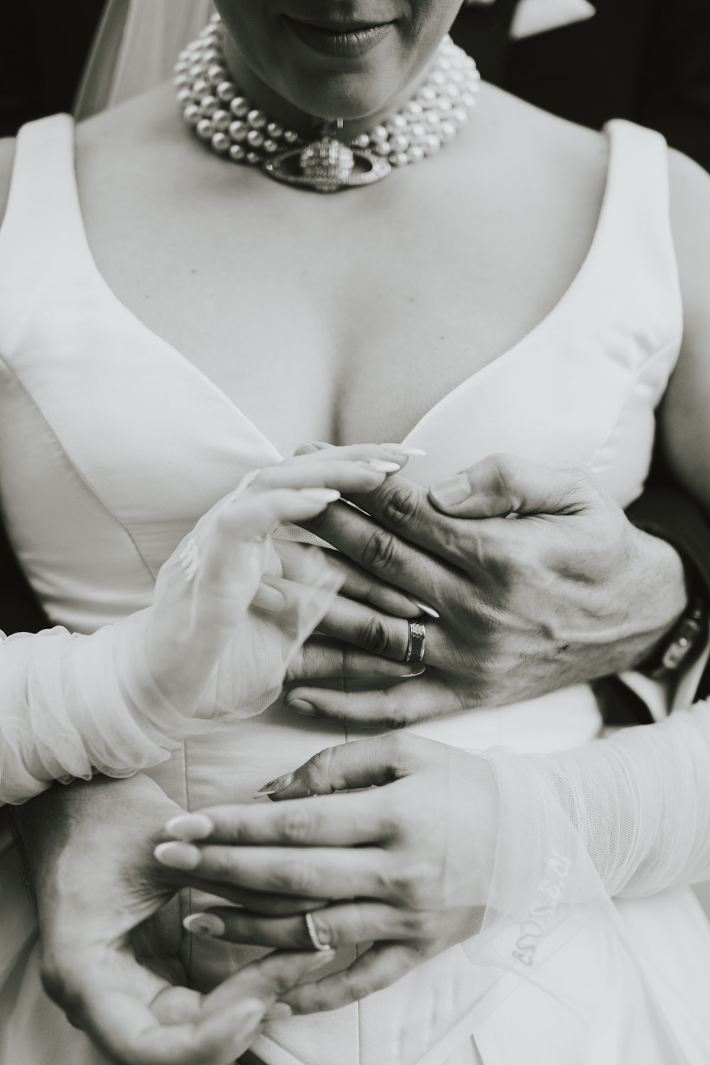 Pearls, gloves and several hands gathered around wedding rings