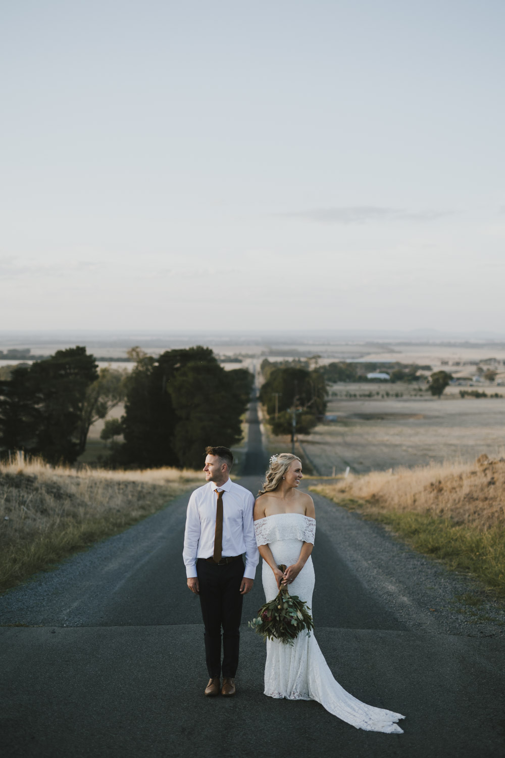 Couple standing on an empty rural road beneath a pale sky
