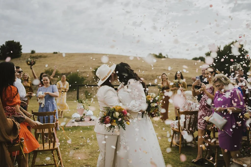 Two brides kissing as confetti fills the air around them