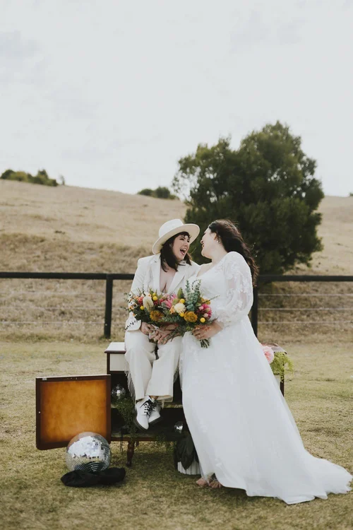 Two brides laughing together in a field