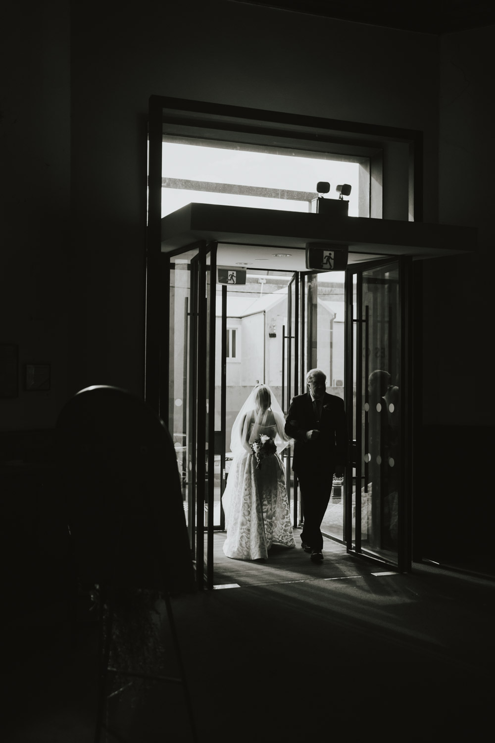 A bride and her father silhouetted as they cross into the ceremony
