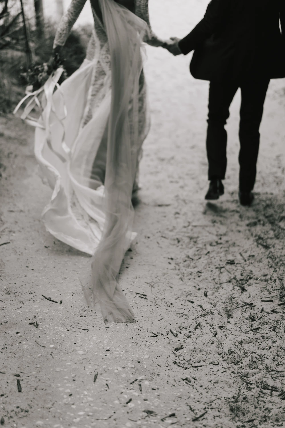 Black-and-white motion detail of the bride's train as the couple walks away