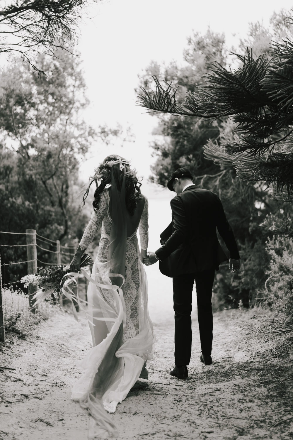 Black-and-white view of newlyweds walking hand in hand down a sandy path