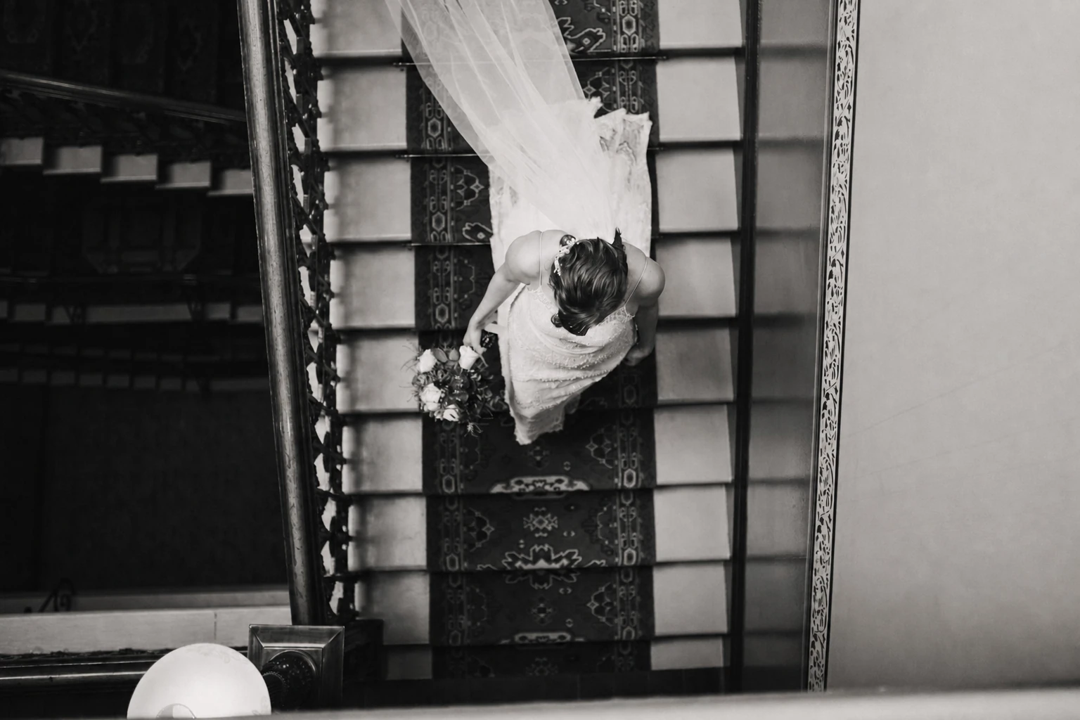 Black-and-white overhead view of a bride descending a patterned staircase
