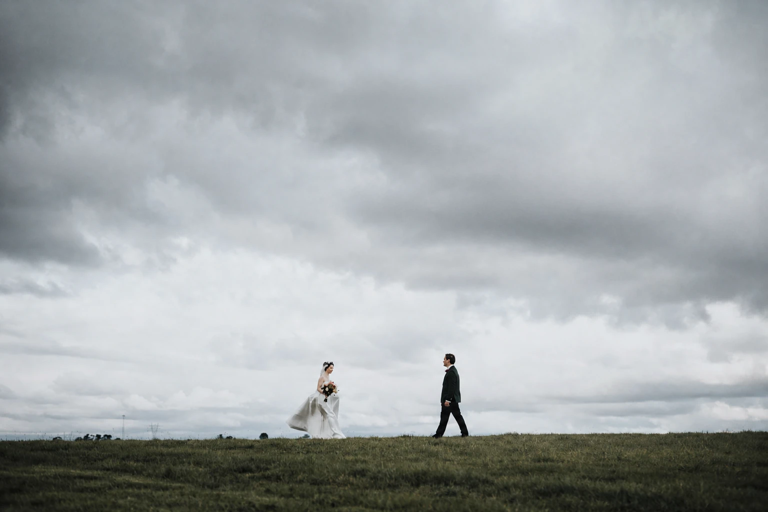 Newlyweds walking toward one another beneath a wide storm sky